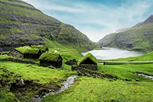 River flowing to the ocean crossing green meadows with grass-roof houses, Saksun, Streymoy Island, Faroe Islands, Denmark, Europe