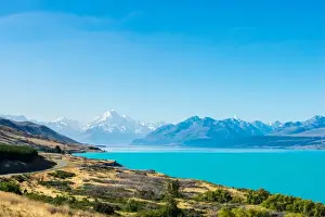 Transport Infrastructure Prints: A road winds along the edge of a turquoise blue lake with mountains in the distance