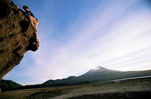 Rock climber attempts bouldering, and volcano in background, Conguillio National Park Rock climber attempts bouldering, and volcano in background, Conguillio National Park