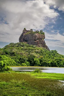 Province Prints: Rock fortress Sigiriya rises above water and lush greenery in central Sri Lanka at midday with a cloudy sky
