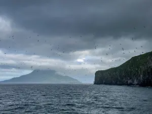 Alaska Prints: Rocky cliffs of Kagamil Island under cloudy skies with distant mountain view in Alaska