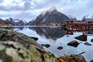 Stillness Prints: Rorbu fishing huts reflect in calm water under cloudy skies in Lofoten Islands Norway