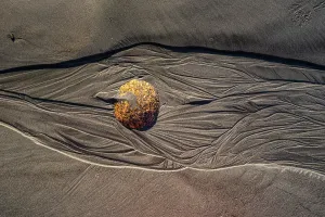 Relax Prints: Rounded stone sits in rippled sand at Cape Foulwind Beach on the West Coast of New Zealand in bright sunlight during