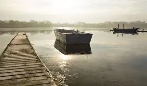 Rowing Boat Prints: A rowing boat floats adrift on a frozen lake beside an empty walkway at Hornsea Mere