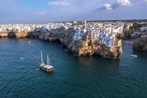 Fishing Village Prints: Sail boat anchored in the water off the white village of Polignano a Mare at sunset