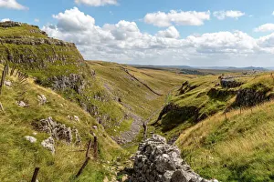 Scenic view of a lush green valley with rocky outcrops under a blue sky with clouds, showcasing natural beauty and tranquility at Malham Cove, Yorkshire, England, United Kingdom, Europe