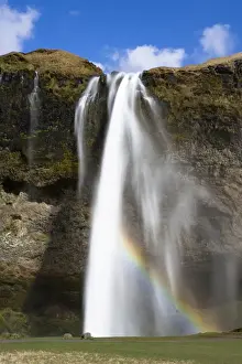 Purity Prints: Seljalandsfoss Waterfall tumbling over towering cliffs in bright sunlight with rainbow at the base of the waterfall