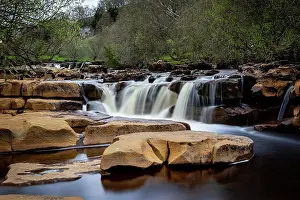Water Feature Prints: Serene waterfall cascading over rocks with lush greenery in the background