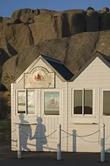 Shadow of couple walking past beach huts in front of granite boulders, Tregastel