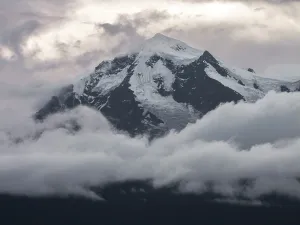 Altitude Prints: Sharp snowy Kawagebo peak in the Meili range at dawn with clouds wrapping around the mountain in soft light