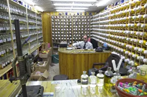 Shelves Prints: Shop owner surrounded by shelves of hundreds of perfume flasks