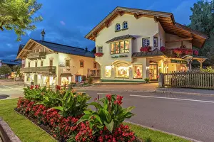 Sidewalk Prints: Shops illuminate the street in Kaprun at dusk during summer in Austria with flowers