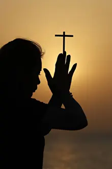 Adults Prints: Silhouette of faithful religious woman praying with Christian cross at sunset