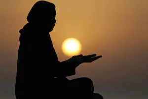 Females Prints: Silhouette of a Muslim woman in abaya praying with her hands at sunset