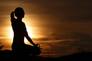 Meditation Prints: Silhouette of a woman in lotus position, practising yoga against the light of the evening