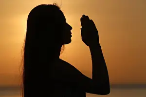 Hands Clasped Prints: Silhouette of a woman standing by the sea at sunset doing yoga pose and meditation, Kep