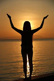 25 29 Prints: Silhouette of a woman standing by the sea at sunset doing yoga pose and meditation, Kep