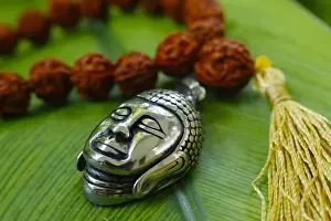 Worshipping Prints: Silver Buddha medallion and prayer beads (mala) on a green leaf, Kep, Cambodia, Indochina