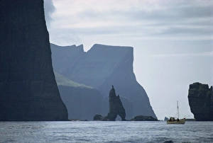 Faroe Prints: Small fishing boat before a towering cliff coastline, Faroe Islands, Denmark