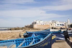 Small wooden fishing boats on seafront with white buildings of the Medina beyond