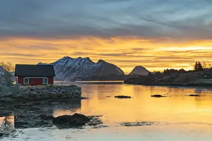 Lofoten Islands Prints: Snowcapped mountains and fishermans red cabin under the burning sky at dawn