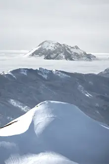 Snowy mountain emerging from fog in the background and snow covered hill in the foreground, Emilia Romagna, Italy, Europe