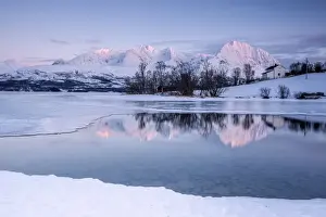 Snowy peaks are reflected in the frozen Lake Jaegervatnet at sunset, Stortind, Lyngen Alps