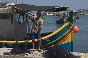 Fishing Nets Prints: Sorting out the fishing net with brightly coloured fishing boats called Luzzus at Marsaxlokk