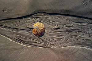 Stillness Prints: Spherical boulder on dark sand with erosion patterns showcases the natural beauty of New Zealand's coastline