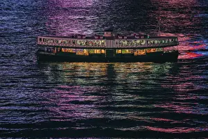 Illuminating Prints: The Star Ferry at night with the reflections of the buildings in the harbour water in Hong Kong