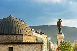Large Prints: Stone building with dome and statue of man holding sword in Skopje against mountain backdrop
