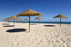 Deserted Prints: Straw umbrellas on empty white sand beach with clear sea behind, Ilha do Farol, Culatra