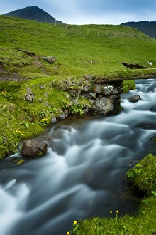 A stream running through the picturesque village of Gasadalur, which is overlooked by the 612m Heinanova mountain, Gasadalur, Vagar Island, Faroe Islands