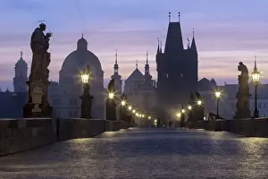 Cobbled Prints: Street lanterns and old statues frame the historical buildings on Charles Bridge at dawn