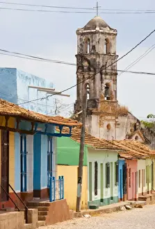 Single Storey Prints: Street scene showing houses painted in bright colours and the ruins of an old church