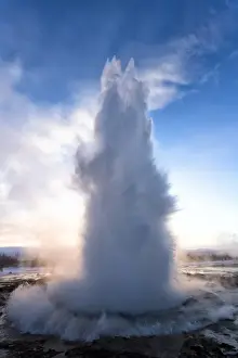 Geyser Prints: Strokkur Geysir erupting at sunrise on a freezing winters morning against the colourful sky