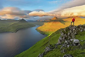 Mid Adults Prints: Summer view of a hiker standing on top of a mountain overlooking the fjord at sunrise