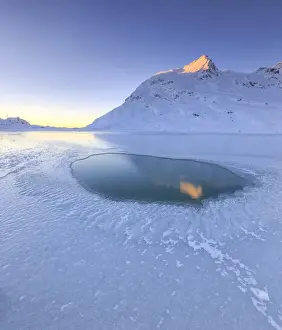 Lago Bianco Prints: The sun illuminating a peak surrounding the frozen Lago Bianco by Bernina