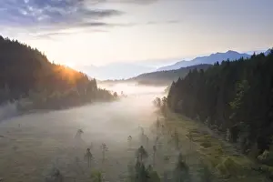 Aprica Prints: Sun rays at sunrise on fog covering the wetland of Pian di Gembro Reserve, aerial view