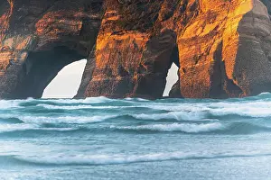 Zealand Prints: Sunlit cliffs of the Archway Islands glow above waves at Wharariki Beach in New Zealand at sunset