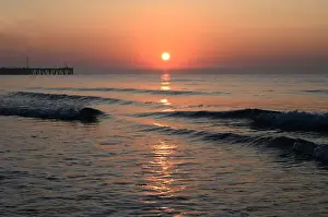 Sunrise over calm sea silhouetting the old derelict harbour wall and groyne, Walberswick