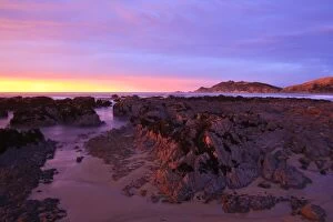 Images Dated 4th April 2009: Sunrise casts a red pink hue on rocks of a beach looking towards Nugget Point, South Island