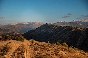 Granada Prints: Sunset over arid hilly landscape in front of the snowy Sierra Nevada