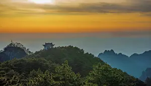 Sunset casts orange and yellow hues over the peaks of Huangshan Mountain in Anhui Province, China, revealing ancient structures and trees