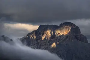 Overcast Prints: Sunset on Croda Rossa d Ampezzo mountains surrounded by the fog and darkness with only a few spots of sun light