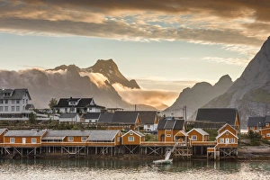 Traditionally Norwegian Prints: Sunset on the fishing village framed by rocky peaks and sea, Sakrisoya, Nordland county