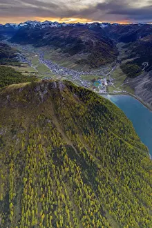 Sunset over larch woods on Crap de La Pare ridge towards Livigno village and lake