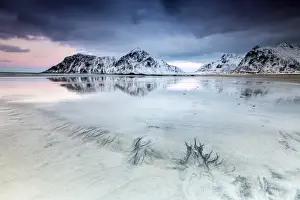 Sunset on Skagsanden beach surrounded by snow covered mountains reflected in the cold sea