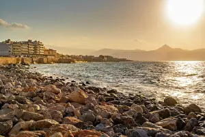 Crete Prints: Sunset view of coastline with rocks and city buildings along shore in Heraklion