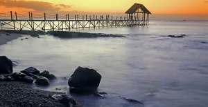 Retreat Prints: Sunset view over a pier with rocks and water in the foreground at Pointe aux Piments in Mauritius during evening hours